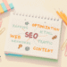 Escritorio de trabajo con cuaderno de notas sobre SEO, lupa sobre post-it rosa, lápices y materiales de estudio organizados, representando diez años de planificación y aprendizaje sobre posicionamiento web antes de lanzar un blog, síndrome del impostor en emprendedoras