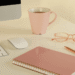 Escritorio de emprendedora con ordenador, taza rosa, gafas y cuaderno representando un espacio de trabajo organizado