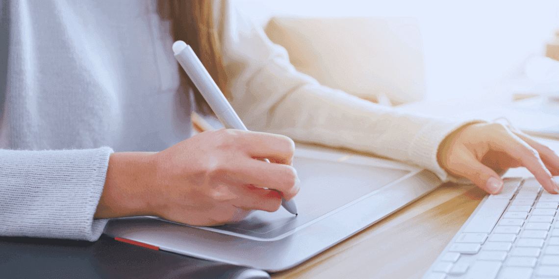 Una mujer escribe con un lápiz digital mientras teclea, diseñando su presencia online.